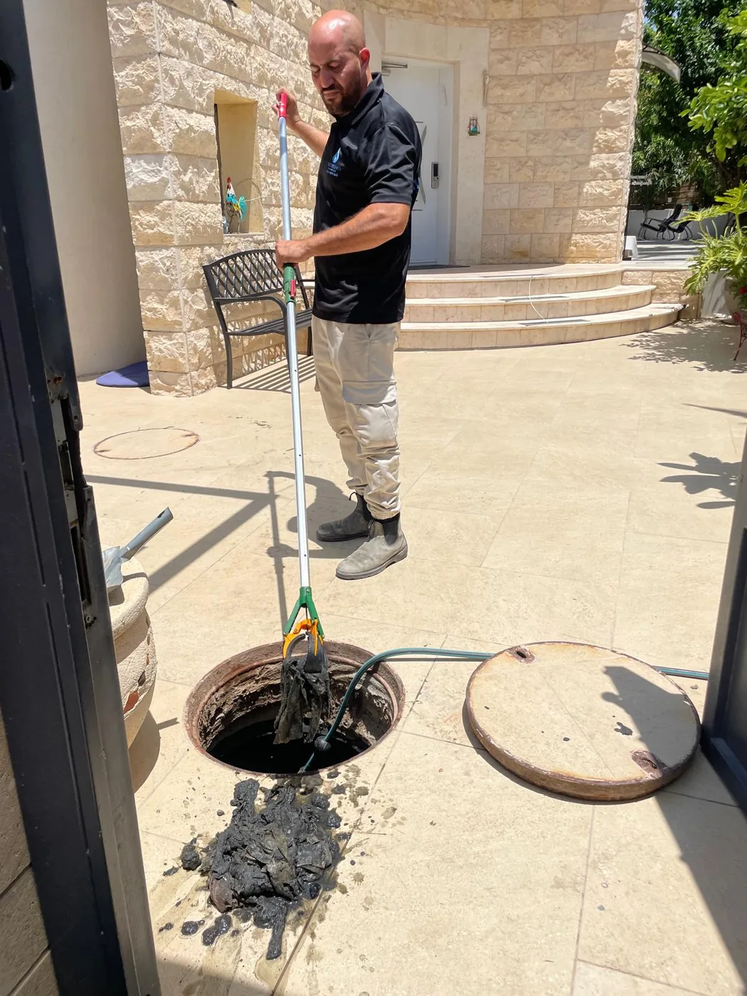 יצחק פותח סתימת ביוב בנס ציונה ומוציא מגבונים תקועים משוחת הביקורת בחצר בית פרטי