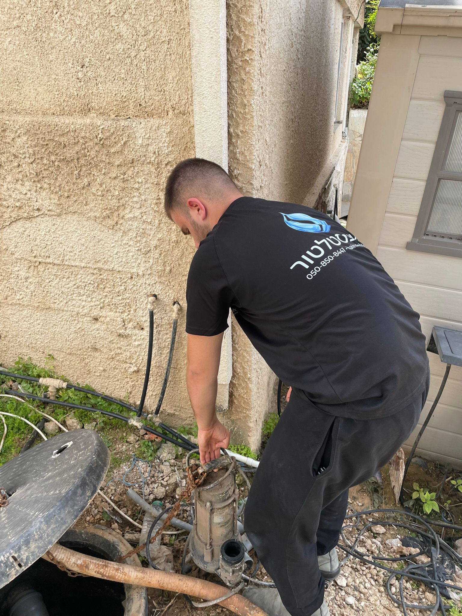 יצחק האינסטלטור מטפל בצנרת חיצונית ובור ניקוז ליד בית פרטי - החלפת קו במרכז